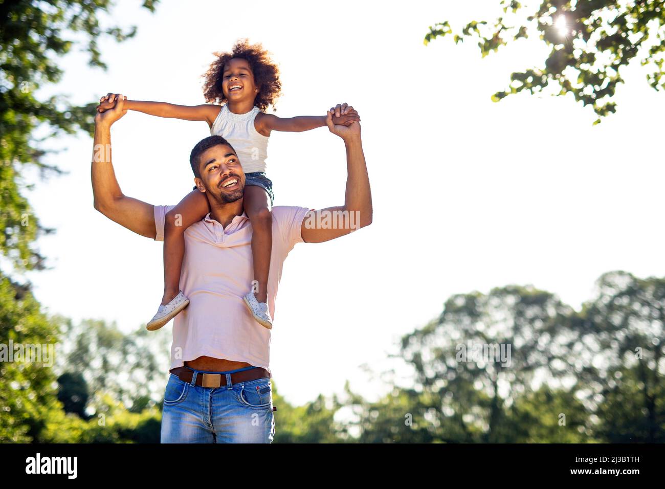 Portrait of happy black father carrying daughter on back outdoors ...