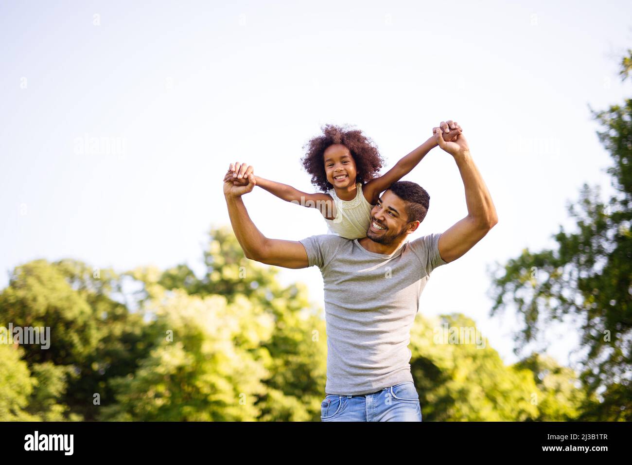 Portrait of happy black father carrying daughter on back outdoors ...