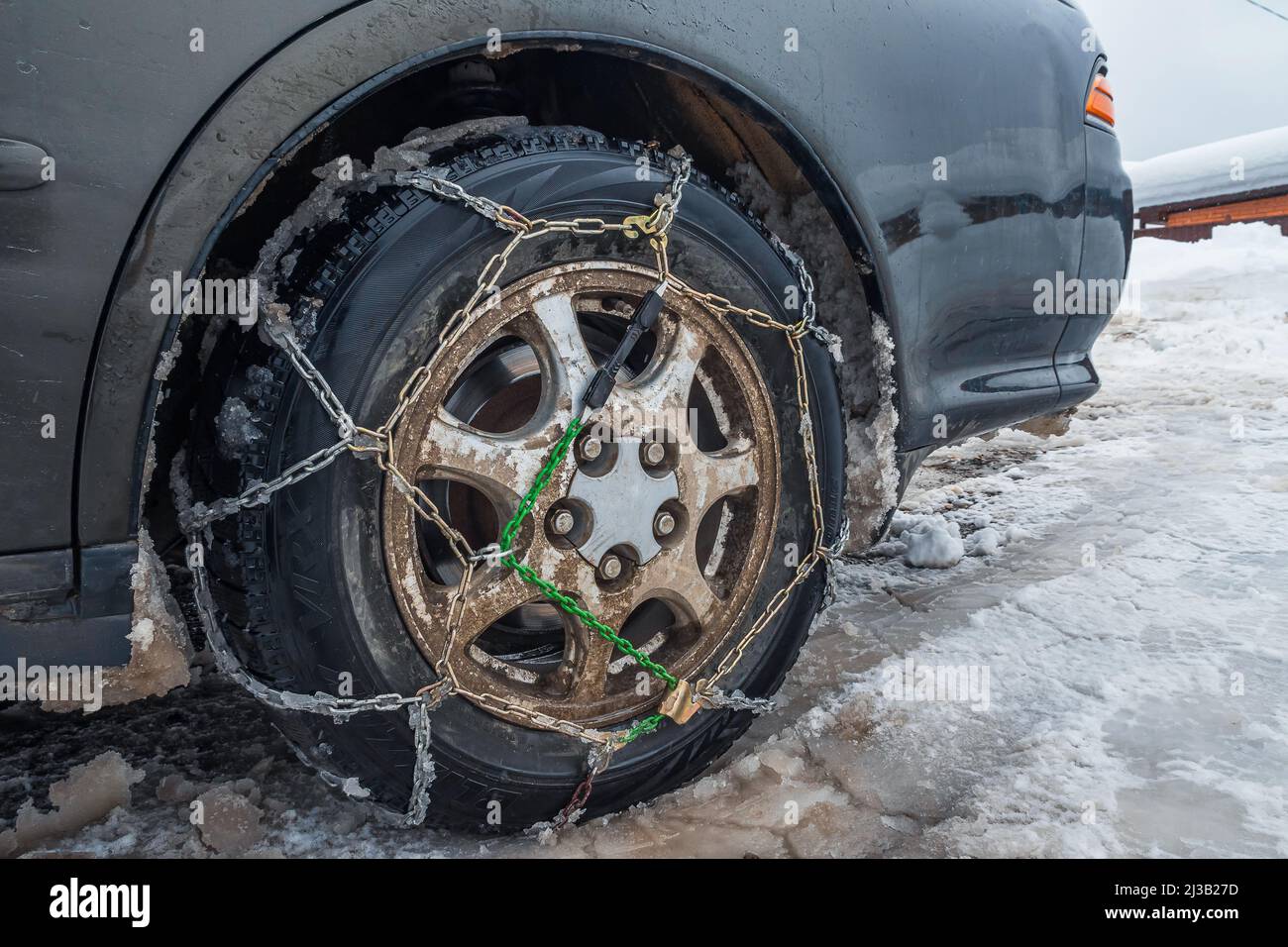 Snow chains on a dirty snowy car wheel. Closeup. The concept of safety