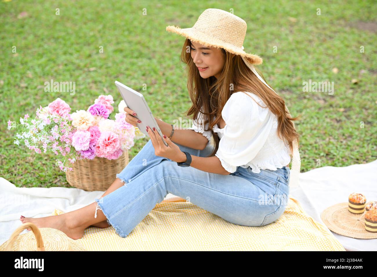 Pretty Asian young woman in a casual outfit and picnic summer hat using portable tablet during enjoy picnic in a nice summer weekend Stock Photo Alamy