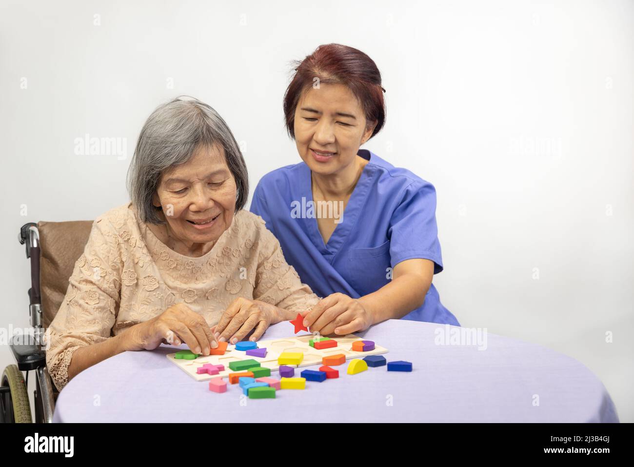 Caregiver and senior woman playing wooden shape puzzles game for