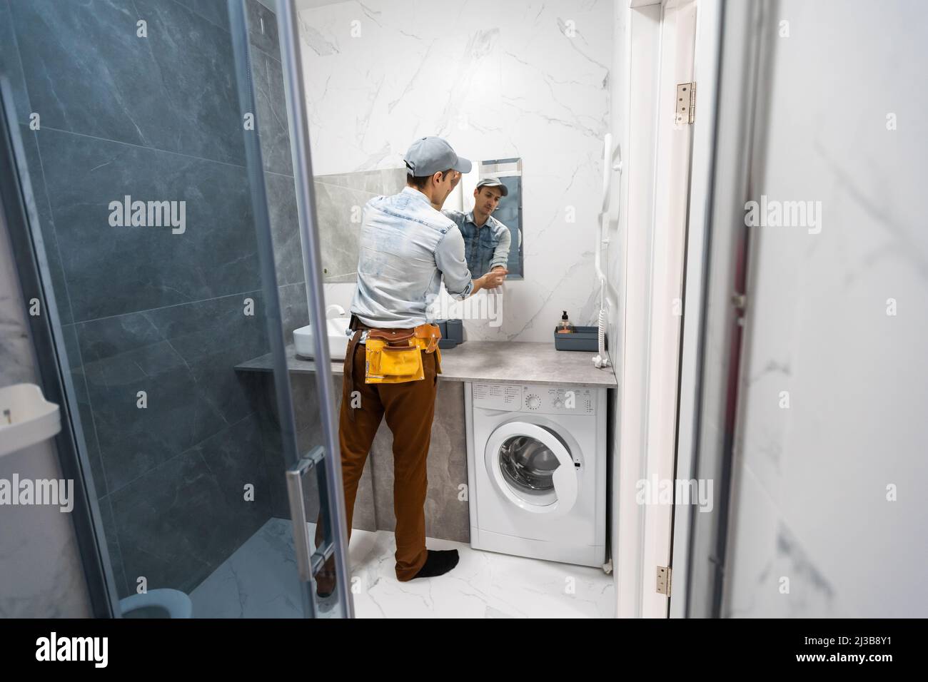 The worker installs the mirror in the bathroom Stock Photo Alamy