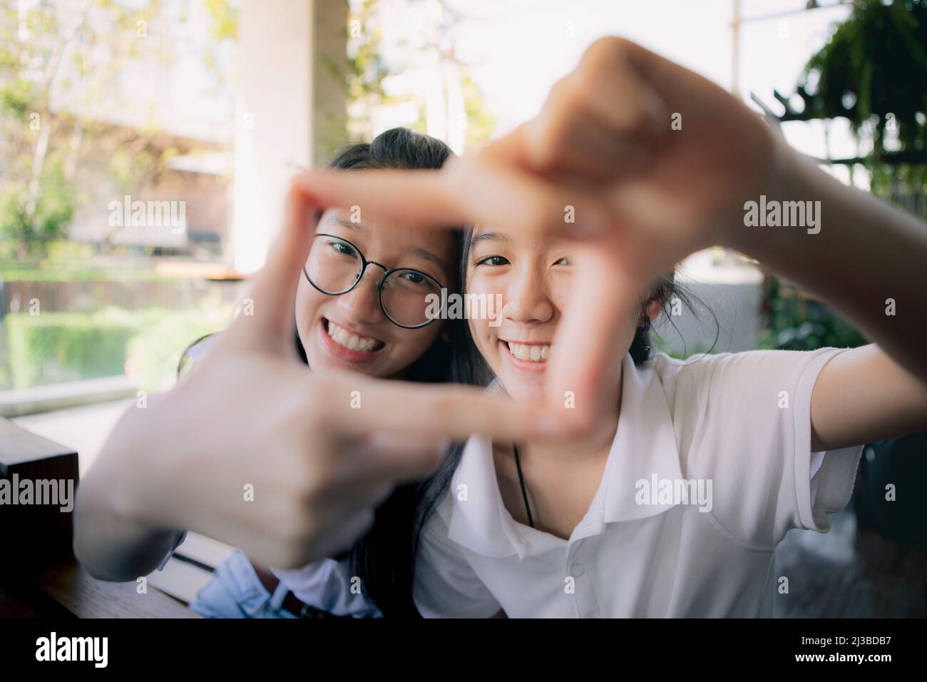 two asian teenager hand sign as photo frame with happiness face behind Stock Photo