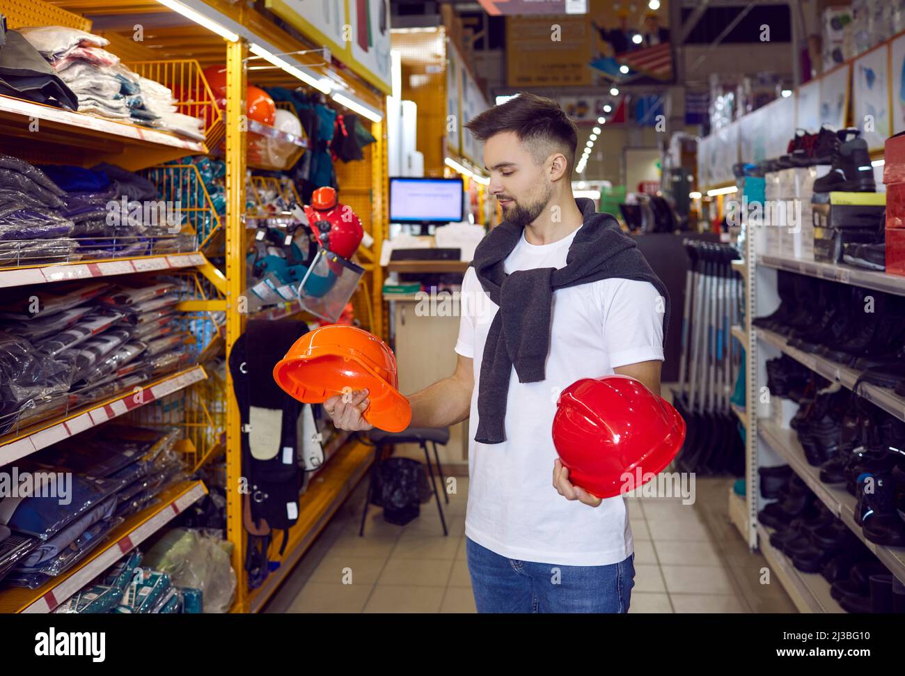 Male customer choosing between two hard hats at a modern DIY store or
