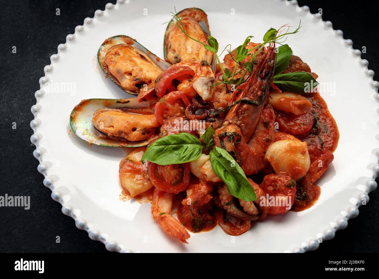 Sauteed seafood with shrimps, mussels, squid and scallop on a white plate, on a dark background Stock Photo