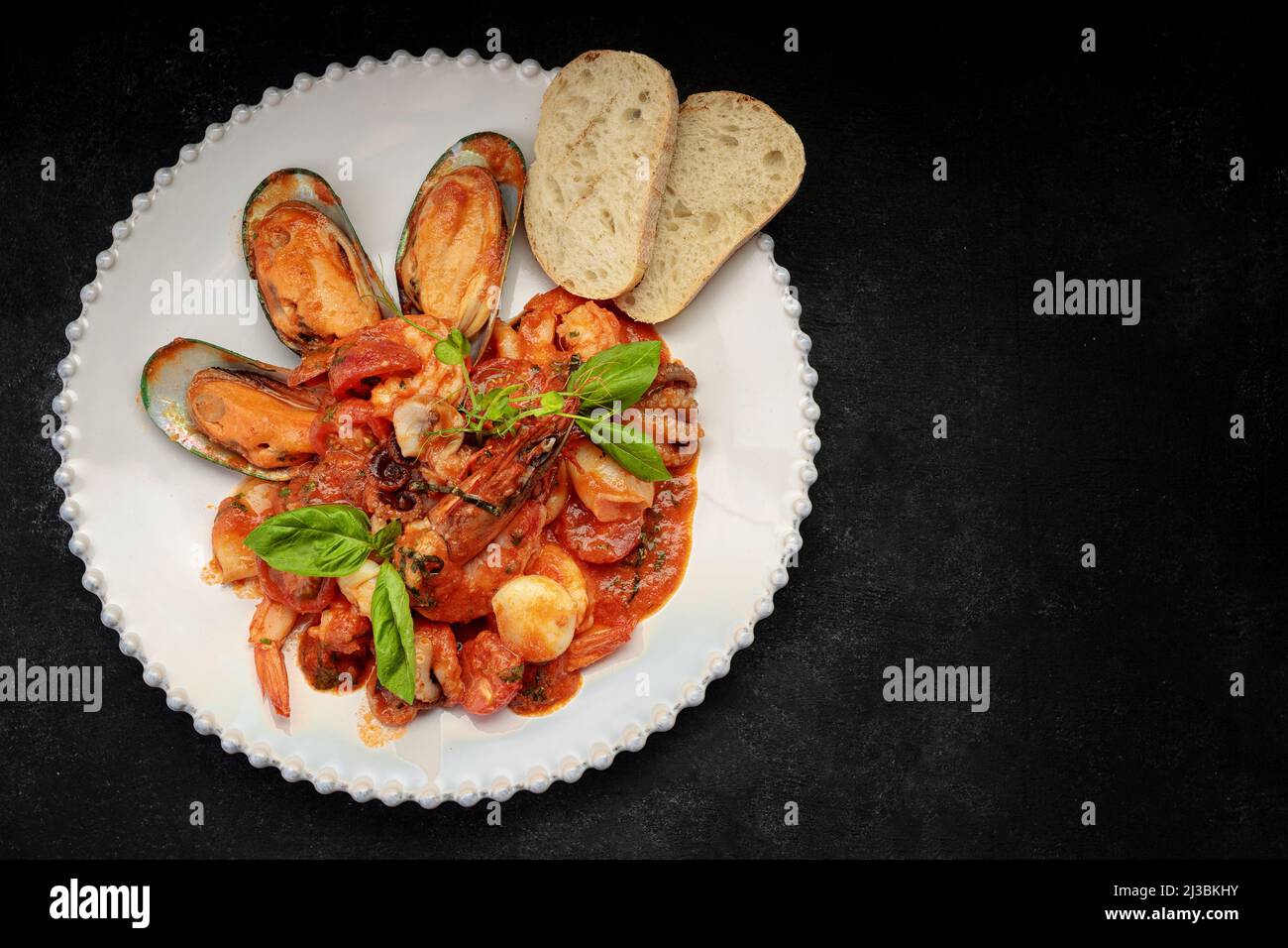 Sauteed seafood with shrimps, mussels, squid and scallop on a white plate, on a dark background Stock Photo