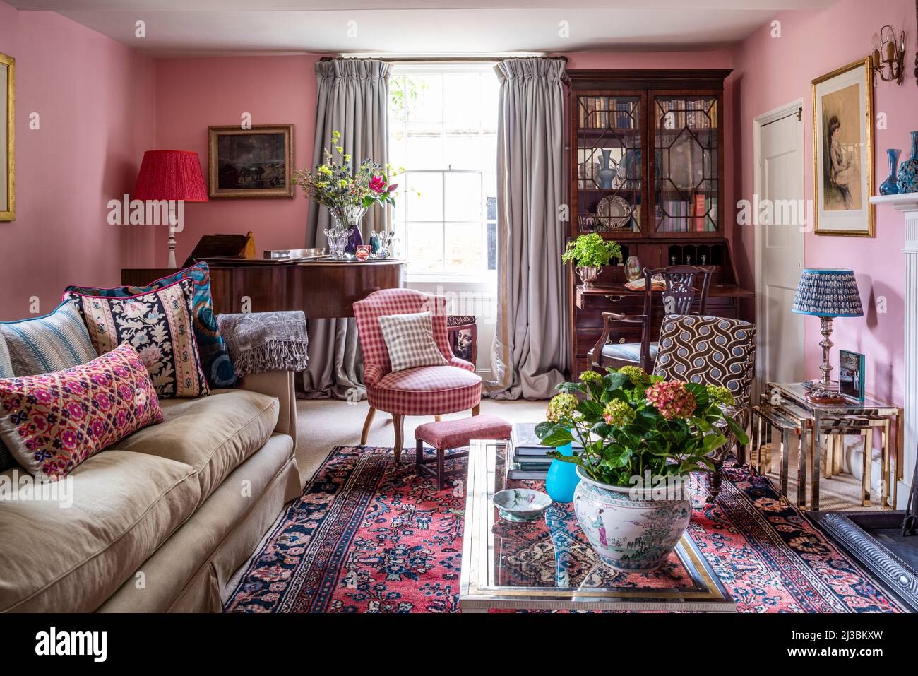 Pink drawing room with piano and bookcase, upholstery in assorted fabrics, 17th century Suffolk home, UK Stock Photo