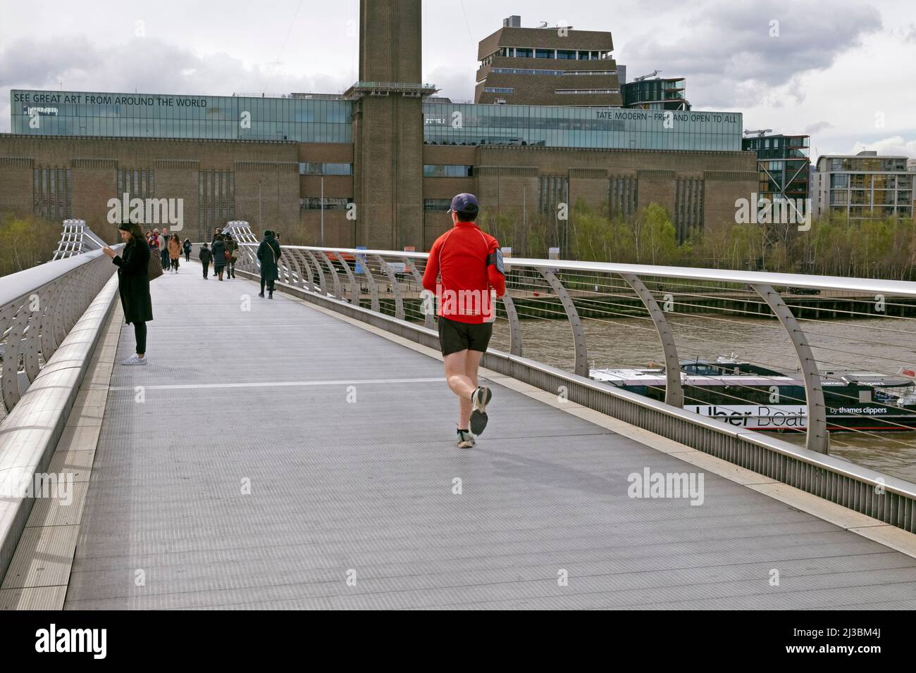 Rear view of man jogger runner running crossing the Millennium Bridge River Thames view of Tate Modern Art Gallery City of London UK  KATHY DEWITT Stock Photo