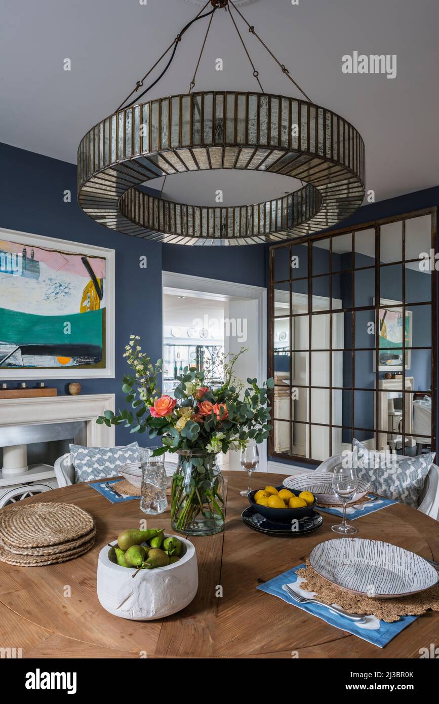 Mirrored pendant above wooden dining table with painting by Matthew Lanyon in renovated St Ives home, Cornwall, UK Stock Photo