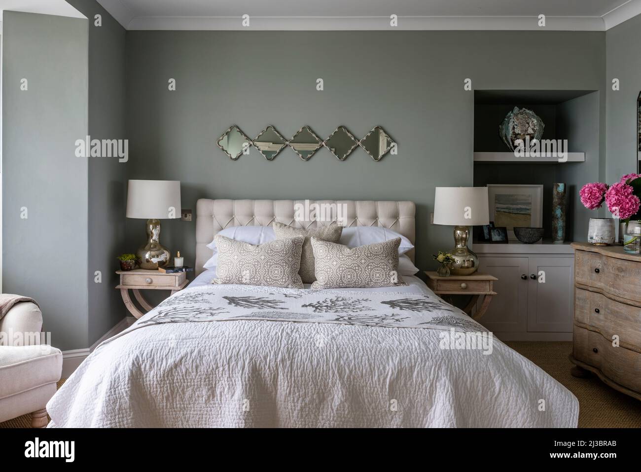 Sage green bedroom with bedside lamps and vintage mirrors in renovated St Ives home, Cornwall, UK Stock Photo