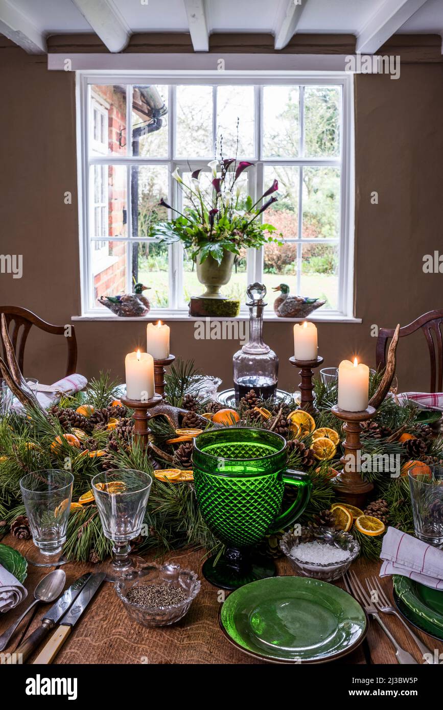 Lit candles with orange and pine centrepiece on dining table at Christmas in 18th century Suffolk cottage, UK Stock Photo