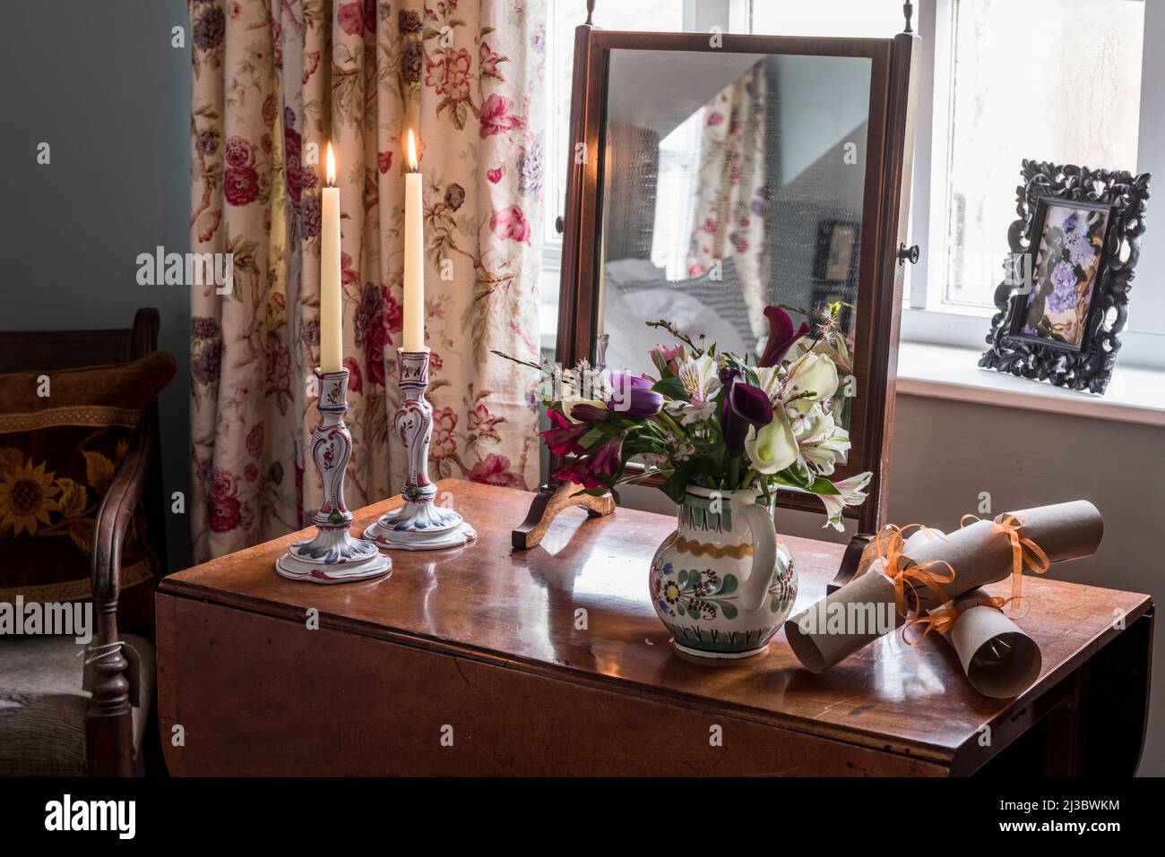 Lit candles and flowers with mirror on drop-leaf table in 18th century Suffolk cottage, UK Stock Photo