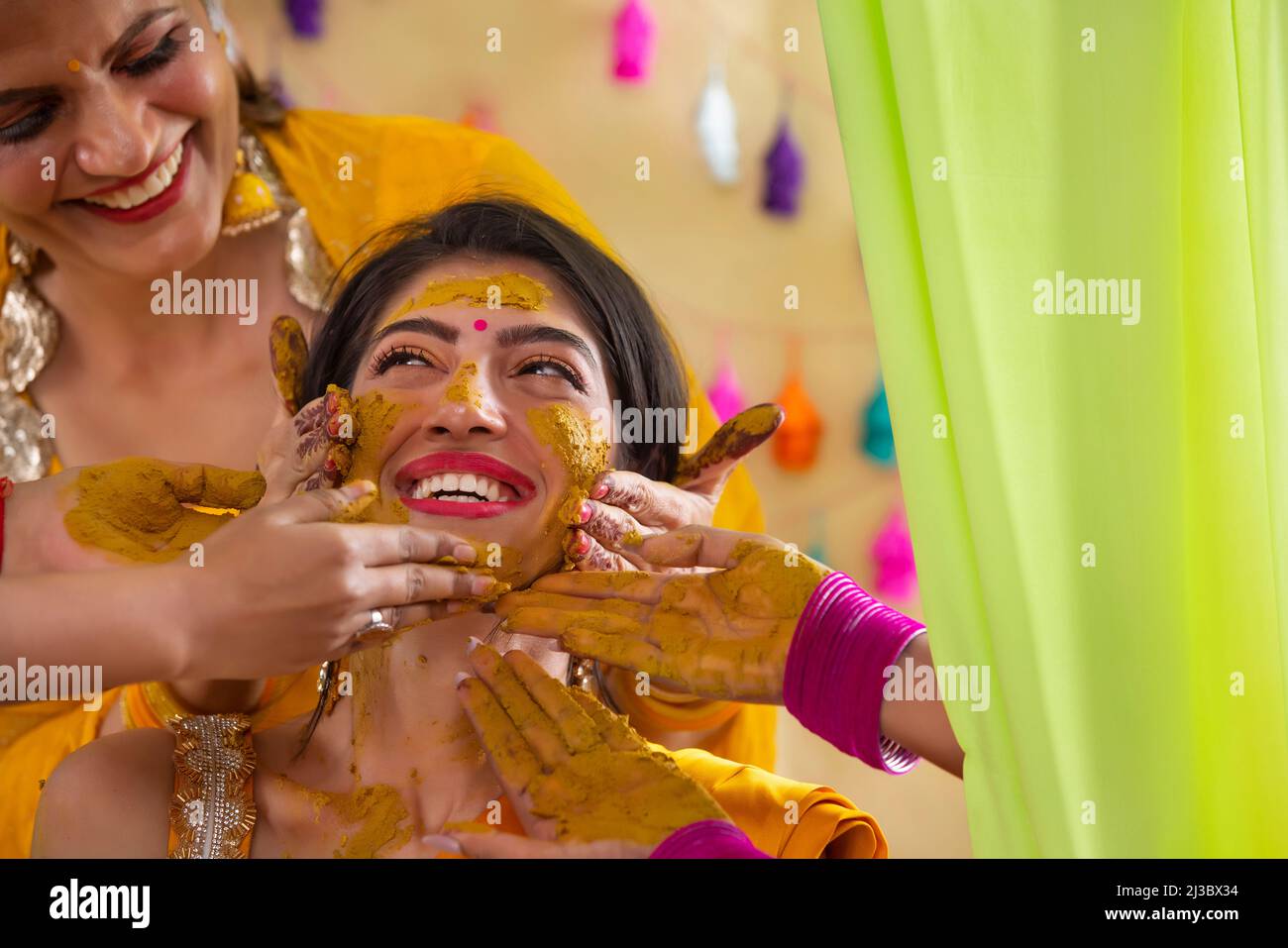 Female hands applying turmeric paste on bride's face on haldi rasam Stock Photo