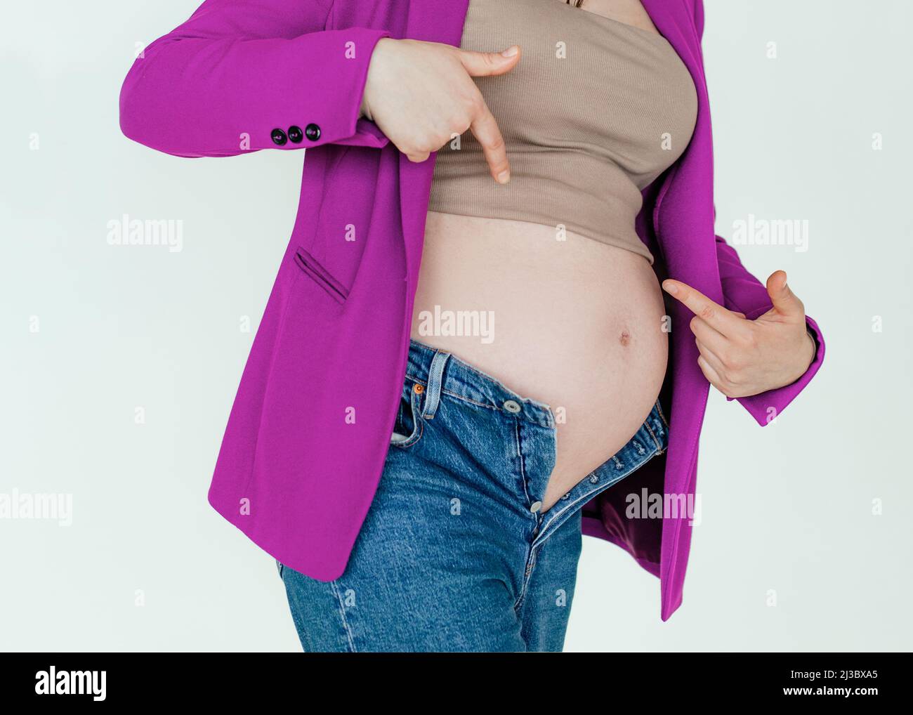 Unrecognizable pregnant woman in not buttoned denim pointing fingers at big belly, problems during pregnancy Stock Photo