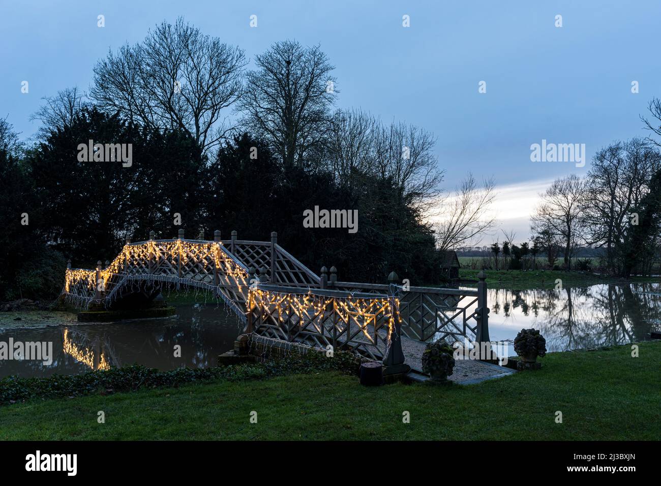 Lit Chinese bridge leading to island in grounds of Island Hall mansion, Cambridgeshire, England, UK Stock Photo