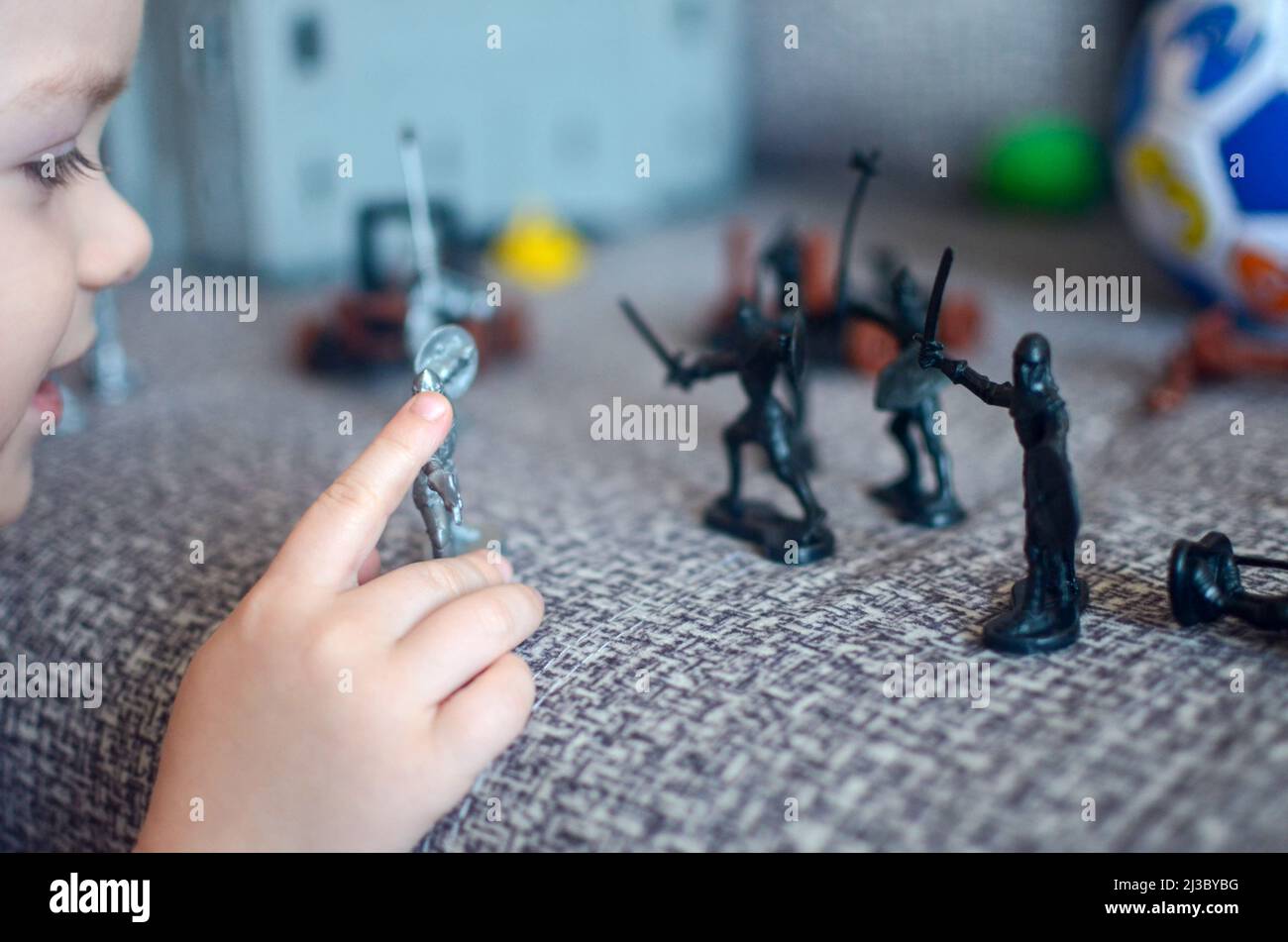 home games for preschoolers concept - caucasian boy's hands and face play toy soldiers on sofa Stock Photo