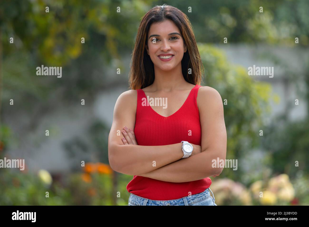 Portrait of a happy woman standing in the park with her hands crossed Stock Photo