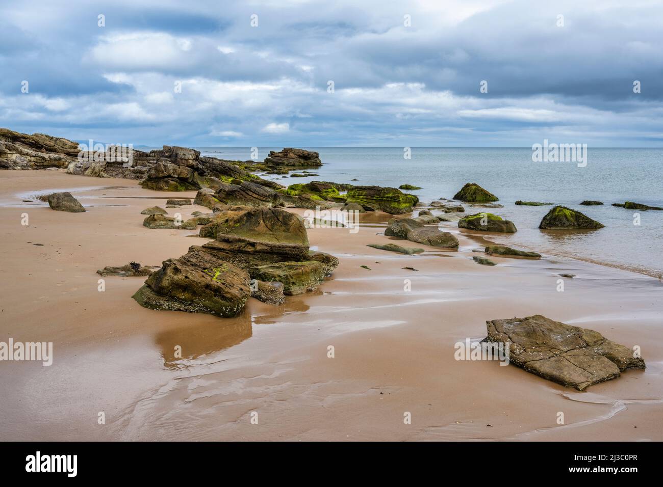 Cluster of rocks uncovered by the retreating tide on Dornoch beach in Sutherland, Highland, Scotland, UK Stock Photo