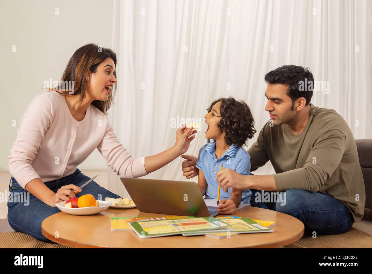 Mother feeding apple to her son while doing homework with father Stock