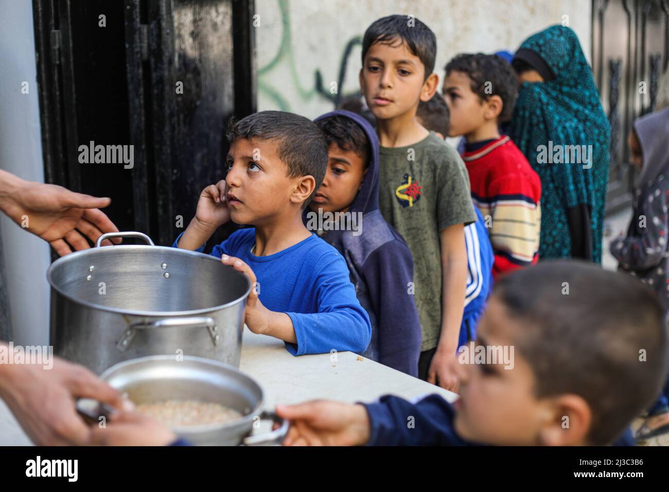 Palestinian children seen in a line with pots and pans to get soup from