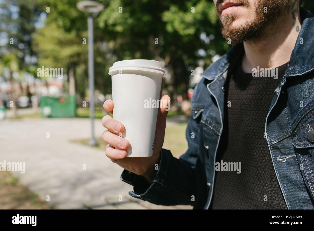Cardboard coffee cup, young man with tattoo on neck holding coffee cup, a sunny park and fun Stock Photo