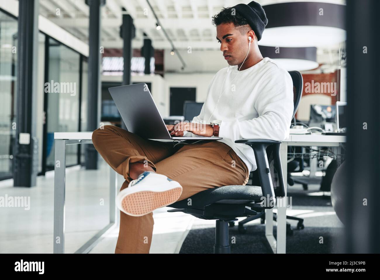 Focused programmer working on a new code. Creative young businessman working on a laptop while sitting alone in a modern workplace. Young businessman Stock Photo