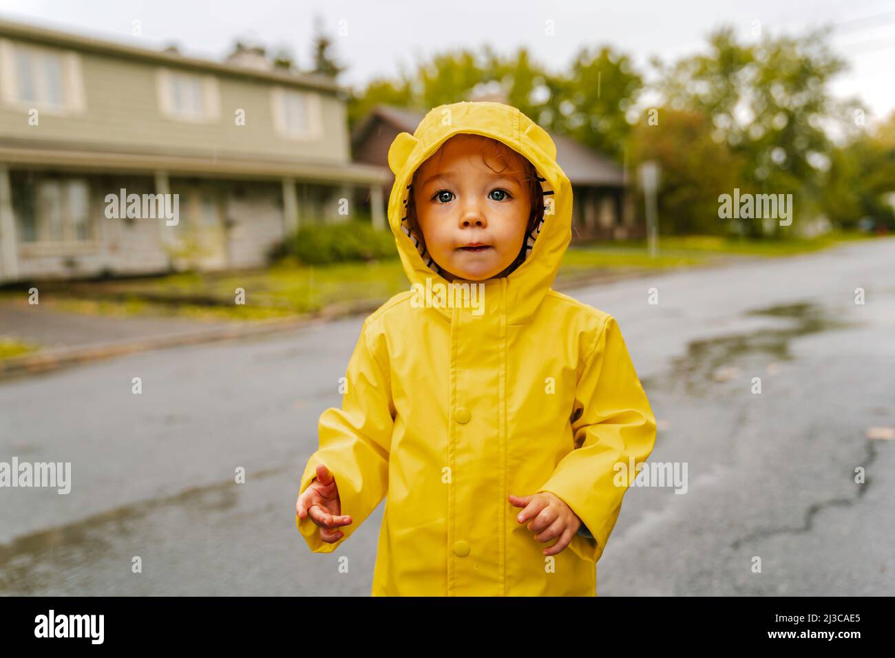 Funny cute baby girl wearing yellow waterproof coat and boots playing