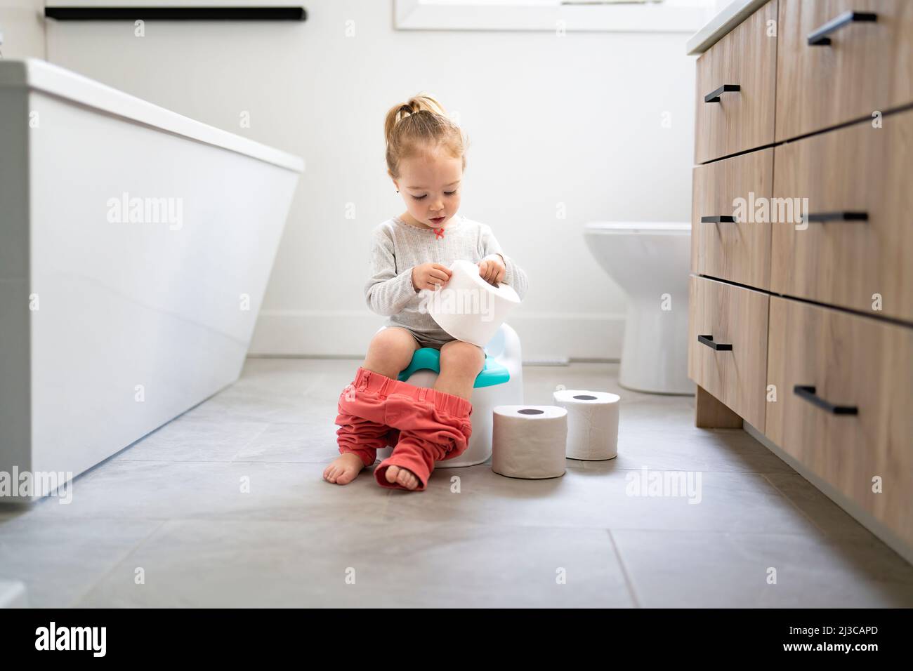 Adorable young baby child sitting and learning how to use the toilet with toilet paper on hand