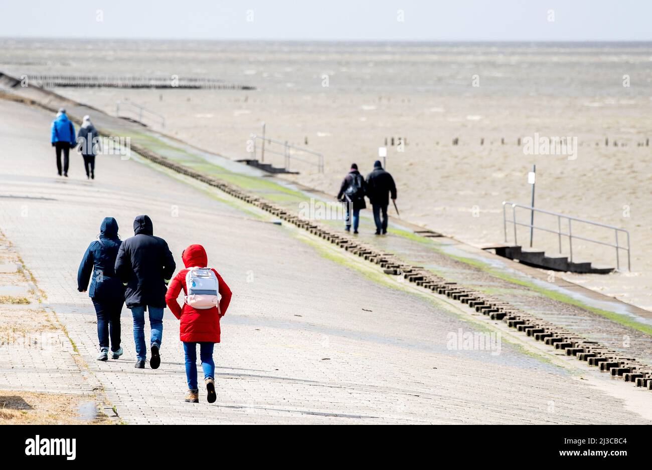 Harlesiel, Germany. 07th Apr, 2022. Tourists walk along the beach promenade at the North Sea in stormy weather. The German Weather Service (DWD) warns of storms, thunderstorms and heavy rain in Lower Saxony. Credit: Hauke-Christian Dittrich/dpa/Alamy Live News Stock Photo