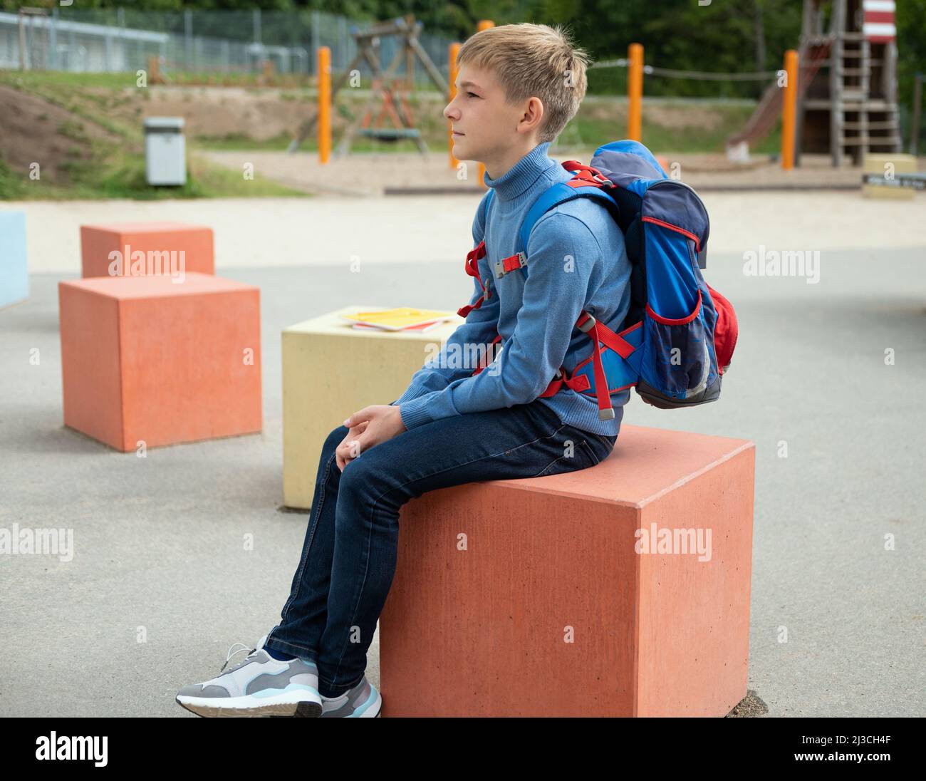 Teen schoolboy with backpack sitting in the school yard after classes Stock Photo