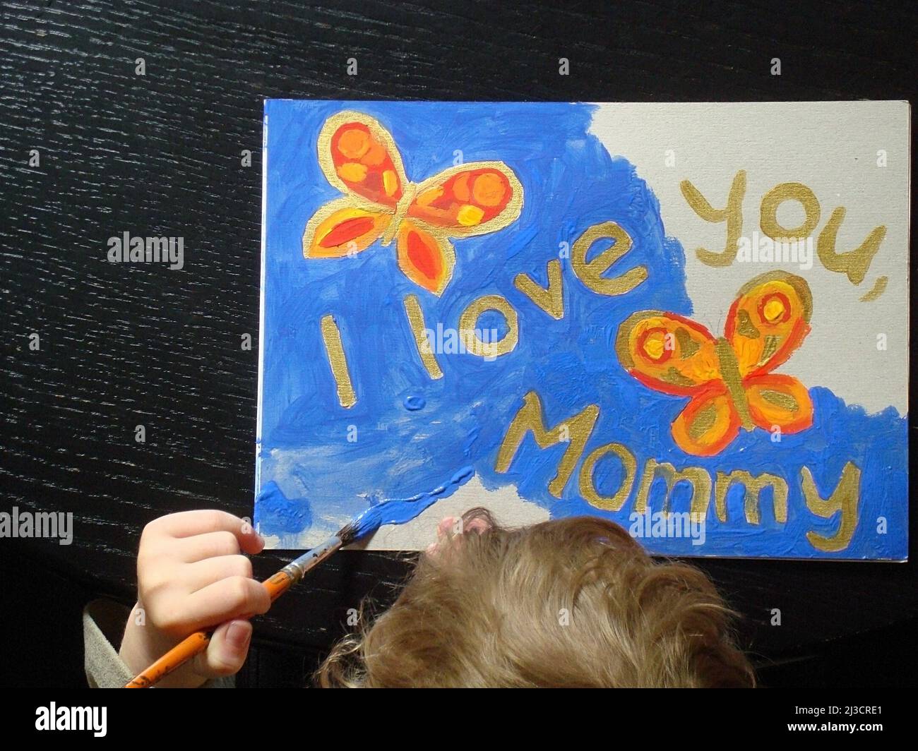 hand of a little child painting a picture with butterflies for mommy at mother's day with the text I love you mommy Stock Photo