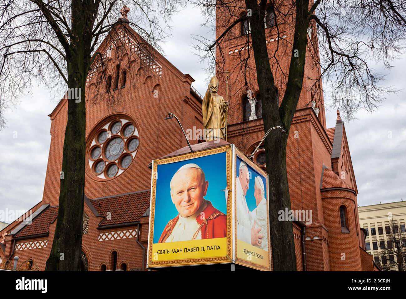 Minsk, Belarus, 04.11.21. Saint John Paul II Pope golden statue in front of Church of Saints Simon and Helena (Red Church) with Pope Benedict XVI and Stock Photo