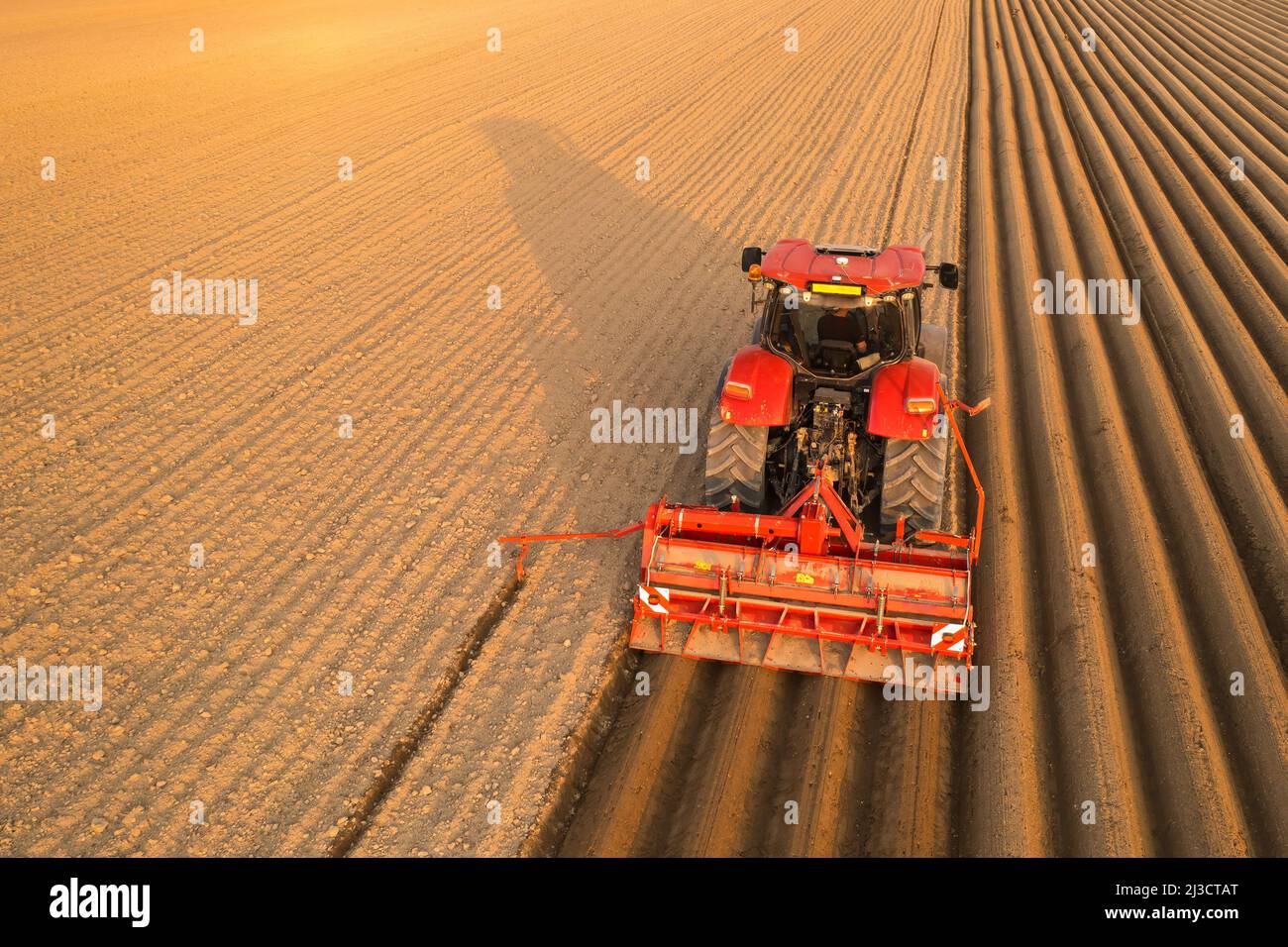 Tractor drags plow for leaving long furrows behind in soil on sunny day