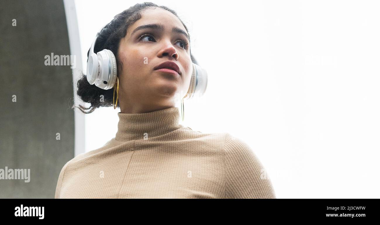 Low angle of Colombian female in turtleneck listening to music in