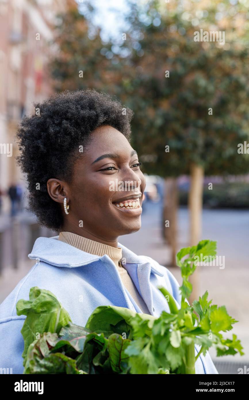 Side view of cheerful African American female with paper bag of fresh ...