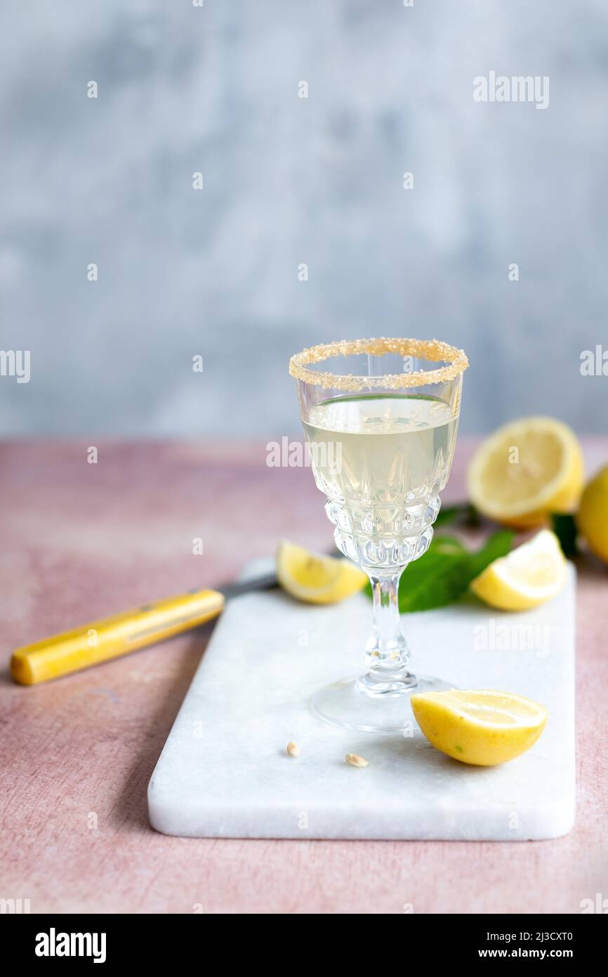 Glass chalice of citrus cocktail with sugar rim placed on marble board near knife and cut lemons in daytime Stock Photo