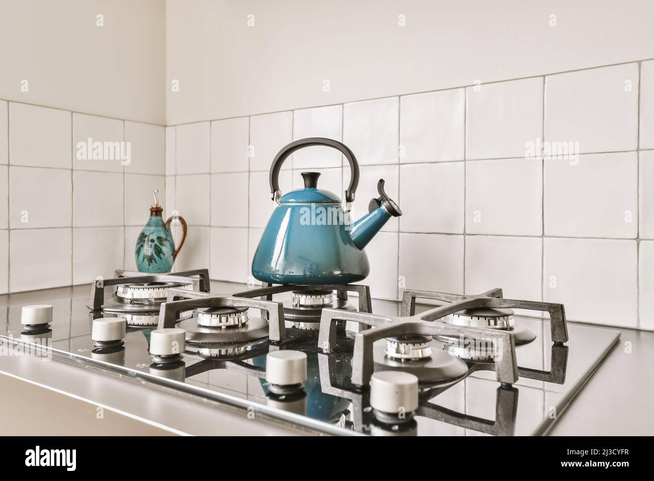 Blue metal kettle placed on gas stove in kitchen with white tiled walls