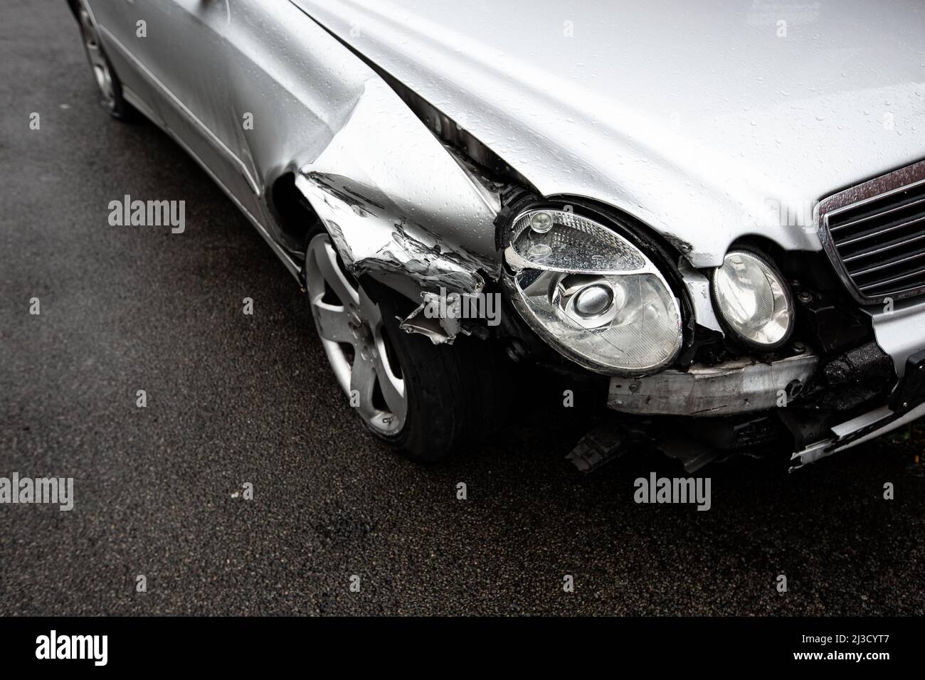 A close up of the damage to a silver car's front wing, wheel and headlights involved in a road traffic accident with copy space Stock Photo