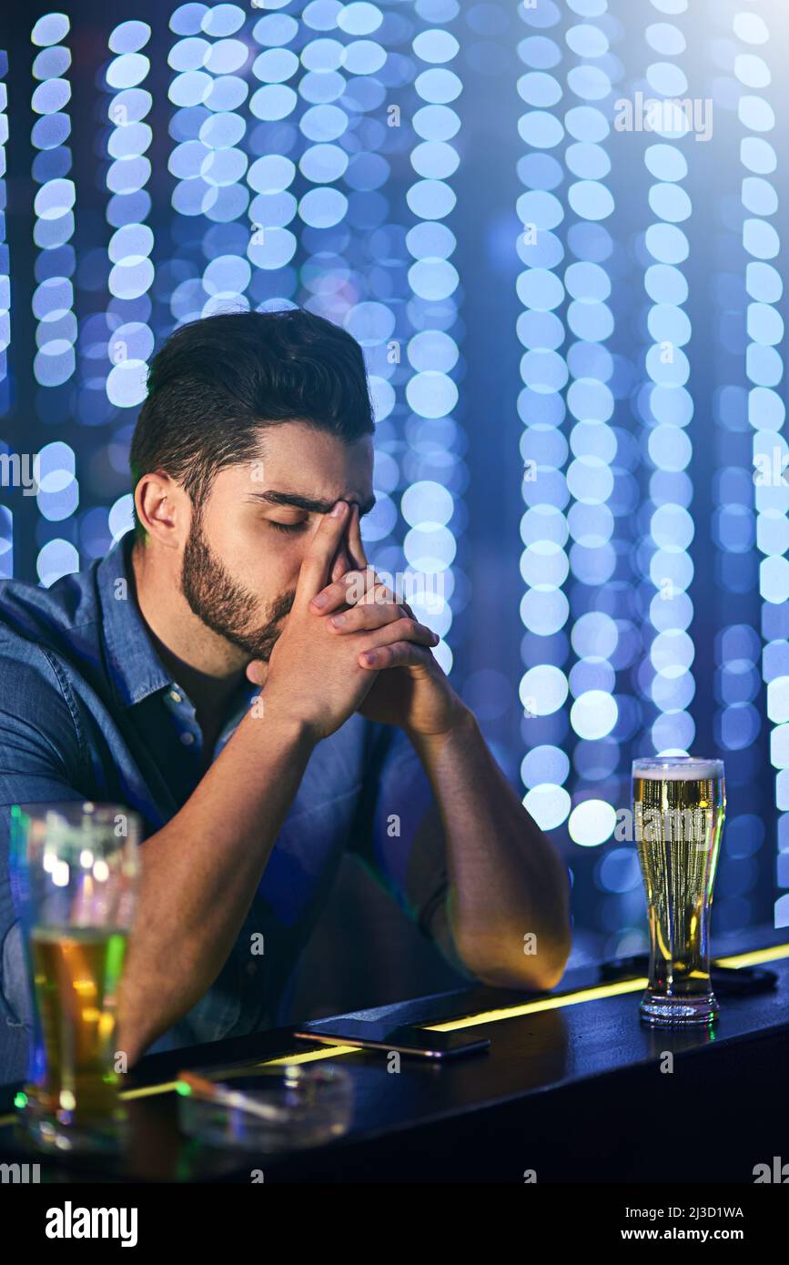 Another night hell never get back. Shot of a young man looking stressed out while having drinks at a bar alone. Stock Photo