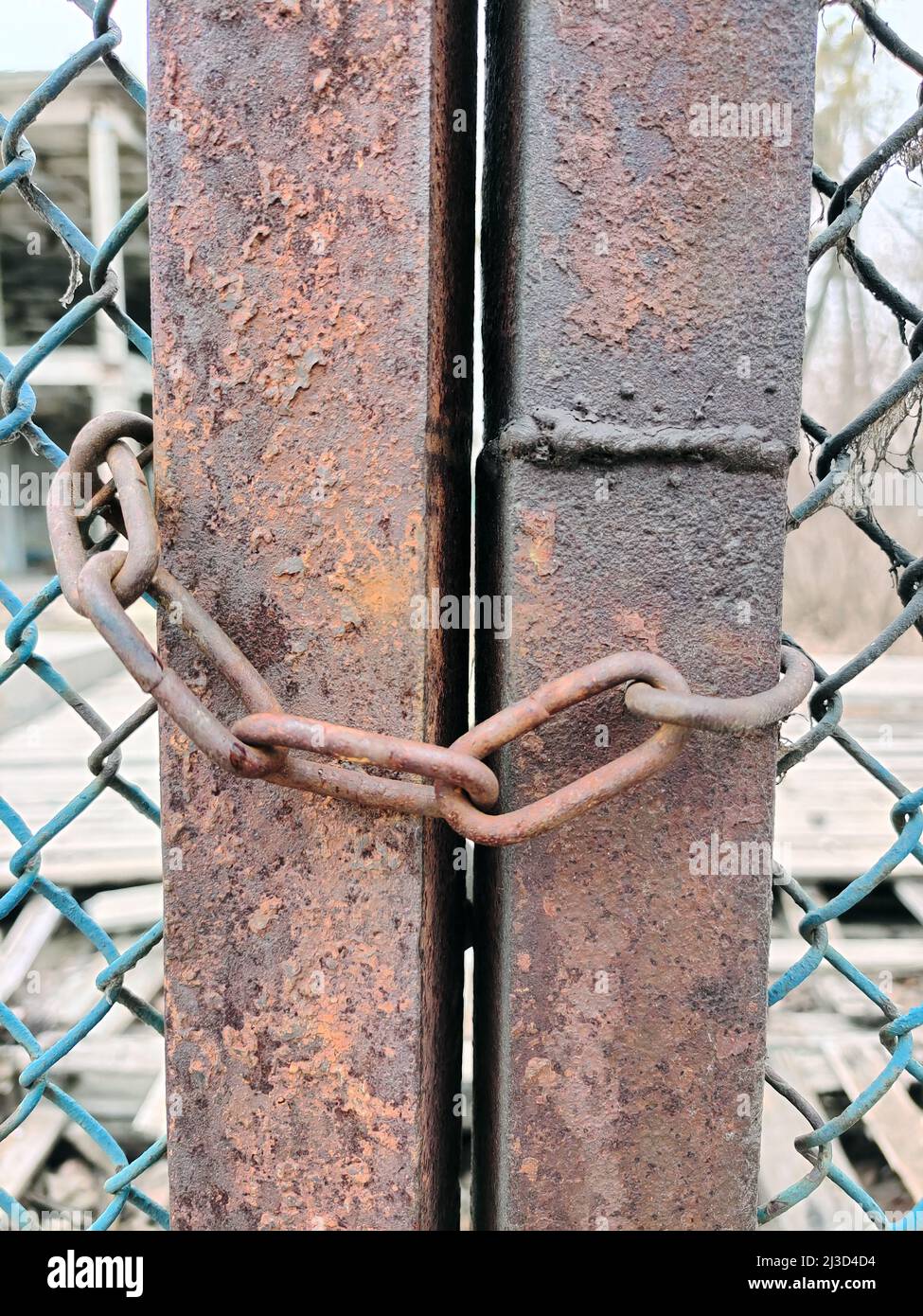 Close-up of a chain hangs on a rusty wire fence. The background is blurry Stock Photo