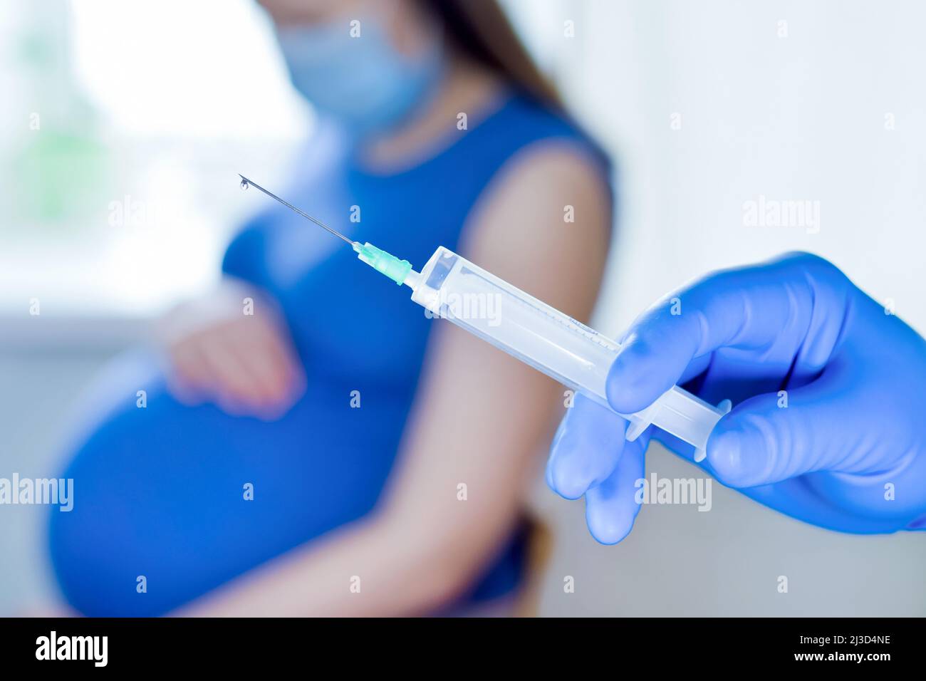  A pregnant woman wearing a blue dress is getting vaccinated by a doctor wearing a blue glove.