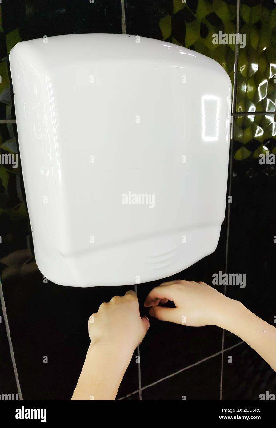 Air automatic hand dryer hangs on the wall and children's hands are dried under it Stock Photo