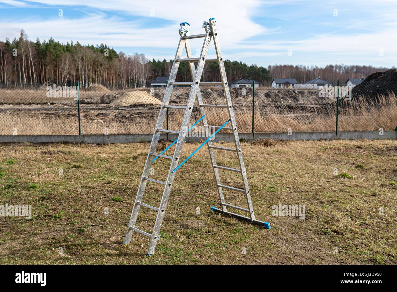 A tall, fold-out aluminum ladder standing in the yard, in the shape of a triangle. Stock Photo