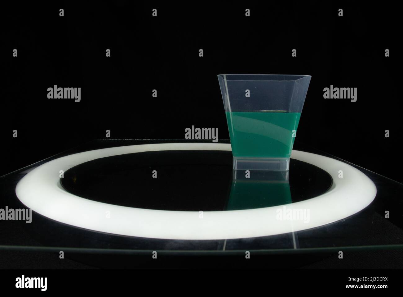 single plastic cup half full of green liquid isolated on a black background in a circle of light Stock Photo