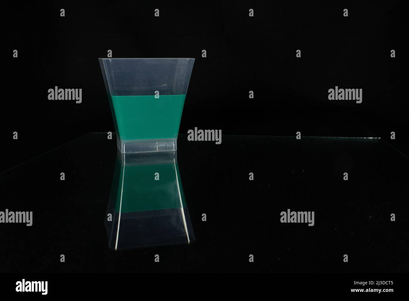 single plastic cup half full of green liquid isolated on a black background reflected in glass Stock Photo