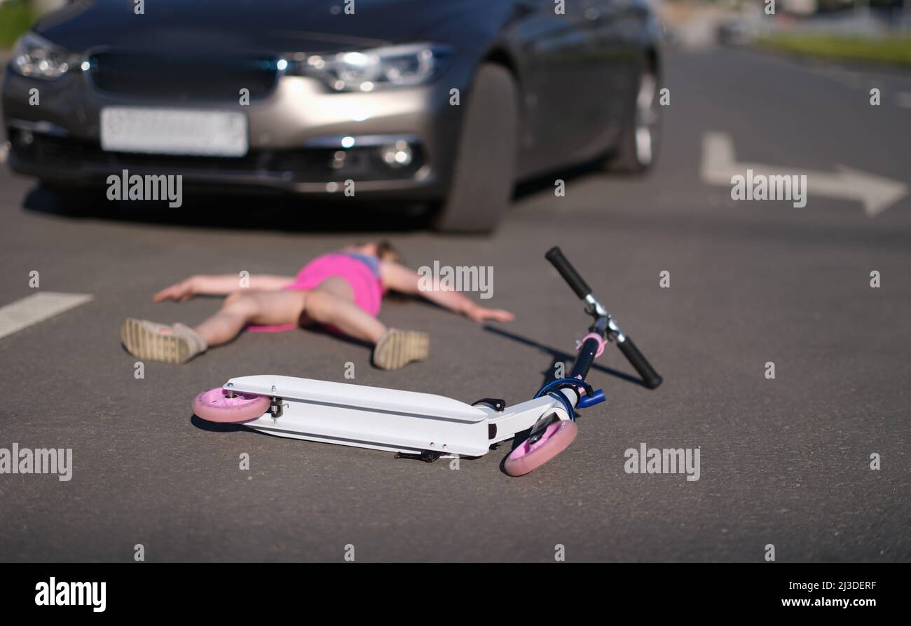 Girl lies on pavement after collision with cars on scooter Stock Photo