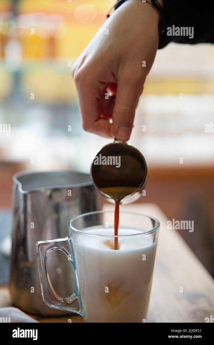 Barista pouring an espresso shot in a cup of foamy milk, making a cappuccino Stock Photo