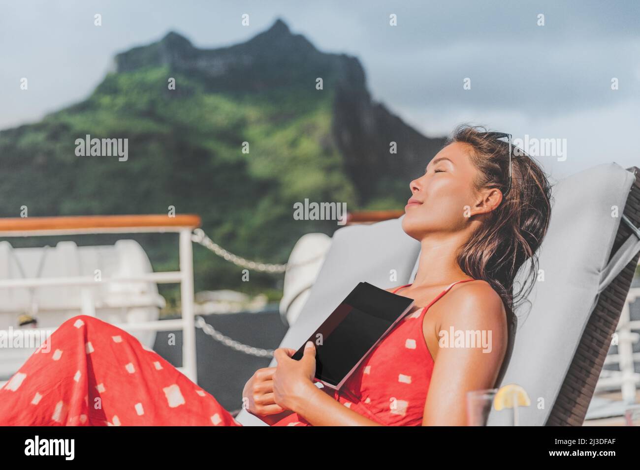 Cruise ship vacation tourist reading book on baconly relaxing in the sun sunbathing on lounger. Happy Asian woman sleeping outside tanning during Stock Photo