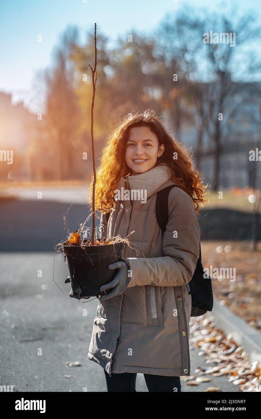 smiling female planting seedling or tree sapling in park to preserve environment Stock Photo