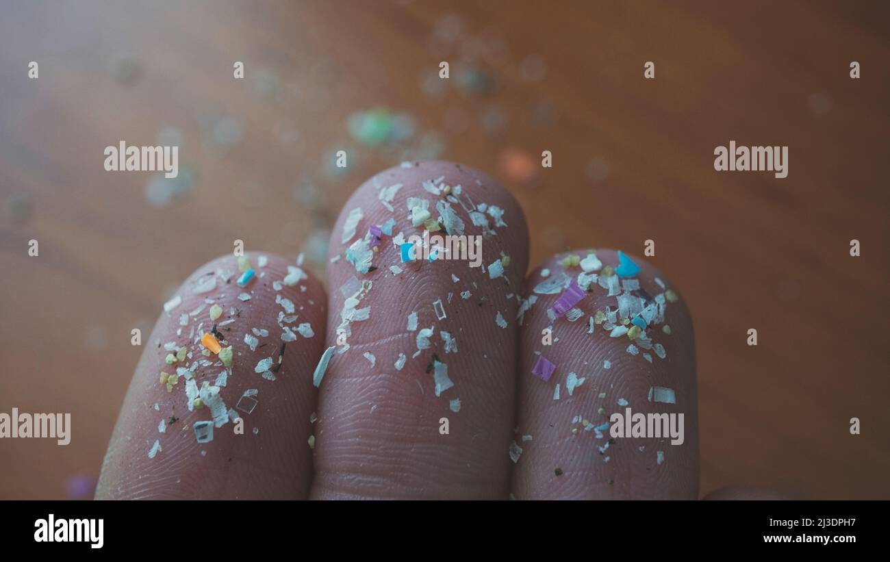 Close-up side shot of microplastics on human fingers. Concept for water pollution and global warming. Climate change idea. Stock Photo